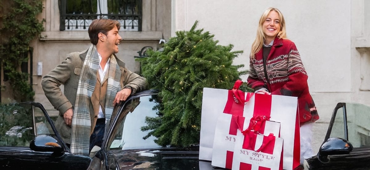 Two people with shopping bags in an urban setting, one holding a Christmas tree.